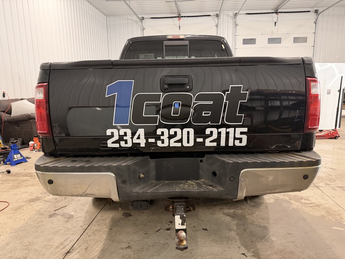Black work truck tailgate with large 1Coat company lettering and phone number
