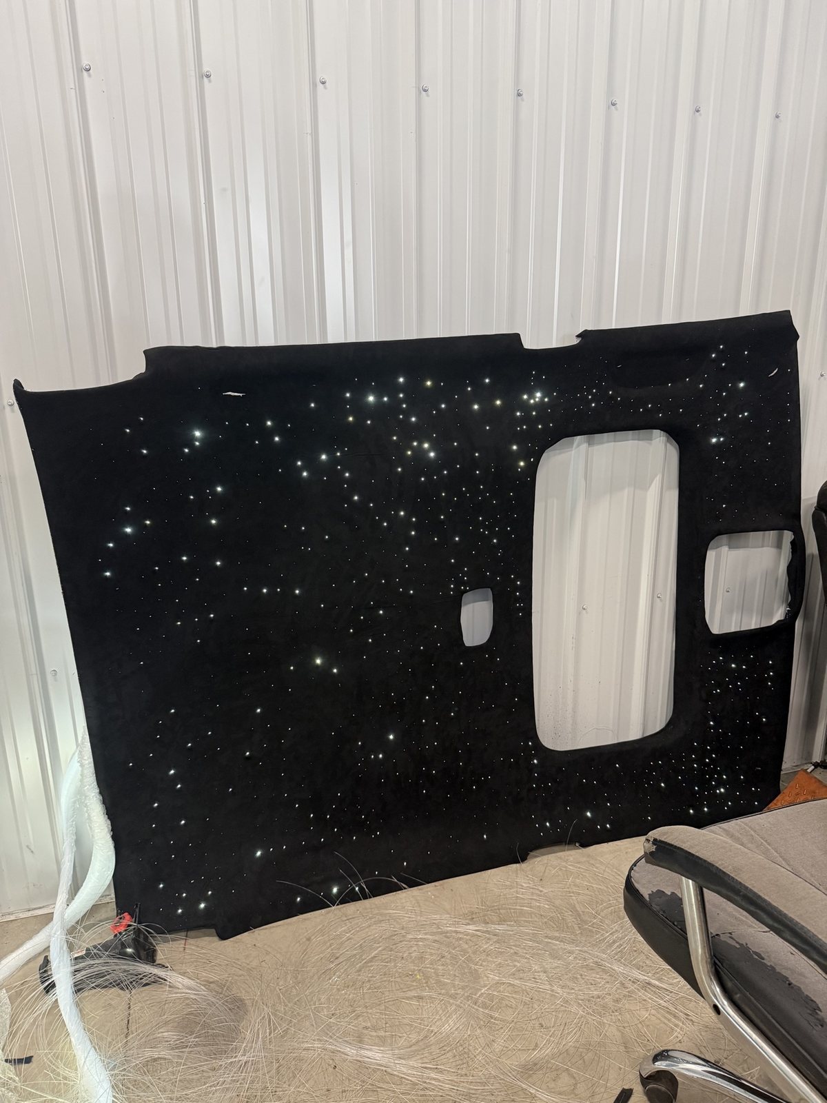 Finished black suede headliner panel leaning in the shop with white stars lit