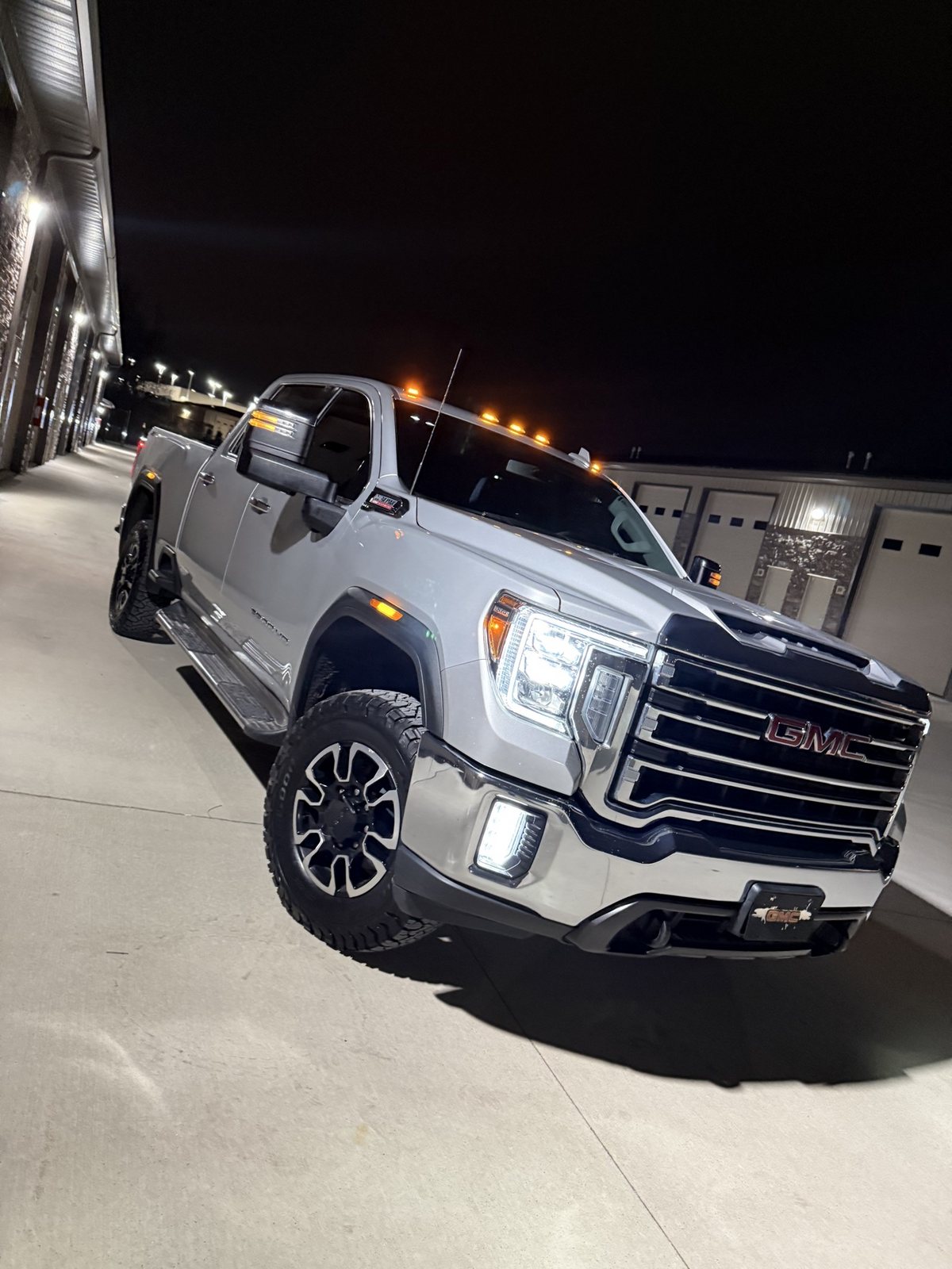 Owner's silver 2020 GMC Sierra 2500HD Duramax front three-quarter view at night with LED fog lights lit