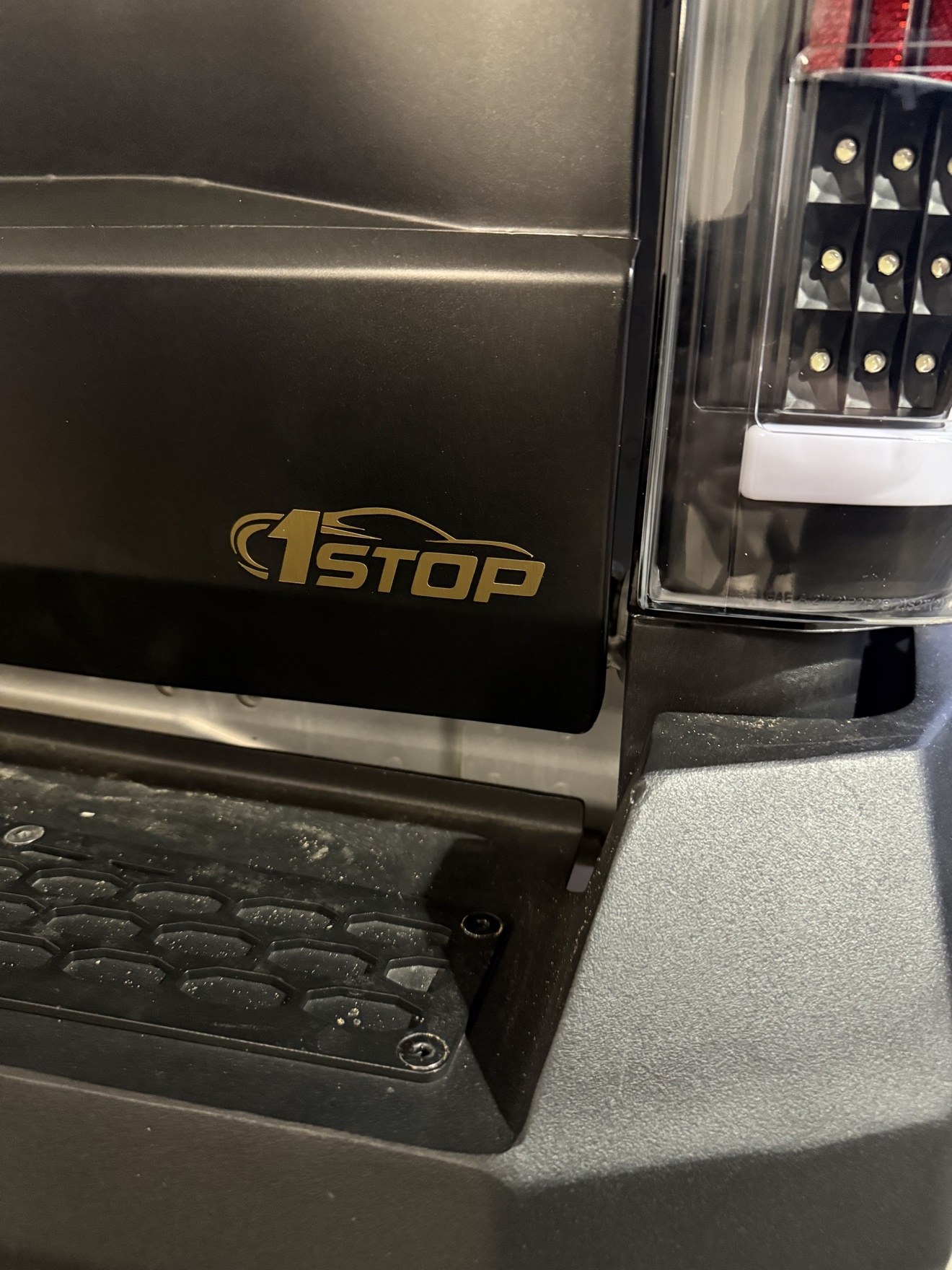 Gold 1Stop Auto Performance decal on the black tailgate of a customer's truck, beside the taillight